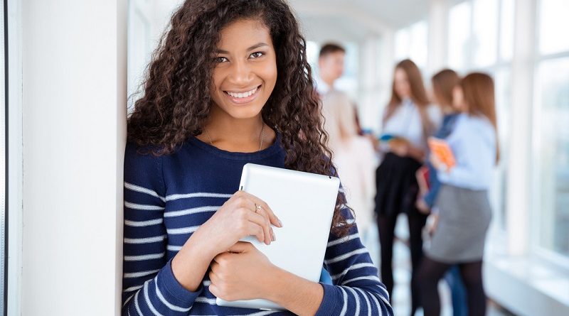 Portrait of a smiling female student standing in university hall with classmates on a background