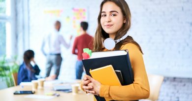 Female student standing in classroom holding books. Portrait of young woman looking at camera indoors