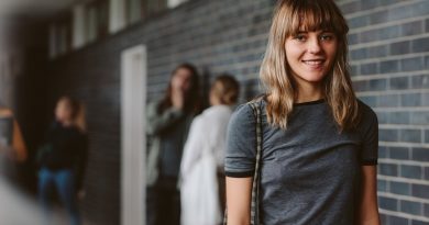 Portrait of beautiful young woman walking in college corridor with students standing in background. Female student in university campus.