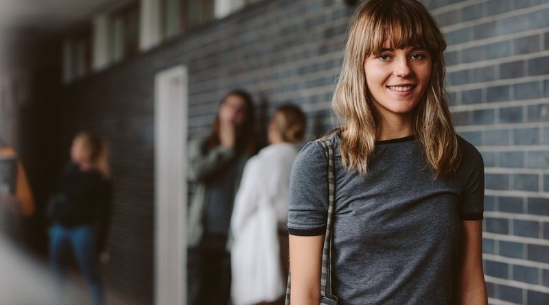 Portrait of beautiful young woman walking in college corridor with students standing in background. Female student in university campus.