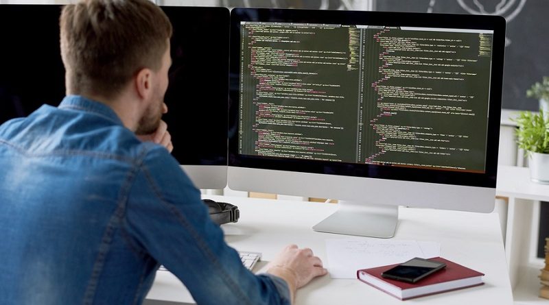 Rear view of concentrated thoughtful male programmer viewing computer language code on computer monitor while working on new program in modern office