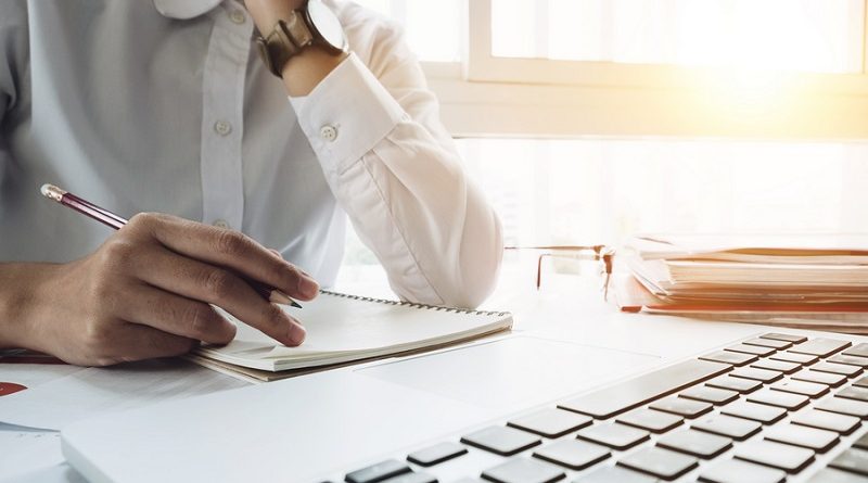 Close up young business woman sitting at table and taking notes in notebook on table is laptop and many books. Student learning online. Blogger.