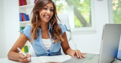 A beautiful smiling young female student is preparing exam and learning lessons in school library, making research on laptop and browse internet.