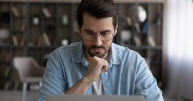 Thoughtful young male manager in eyeglasses looking at laptop screen, considering problem solution, preparing research report, analyzing sales statistic, developing strategy, working on online project