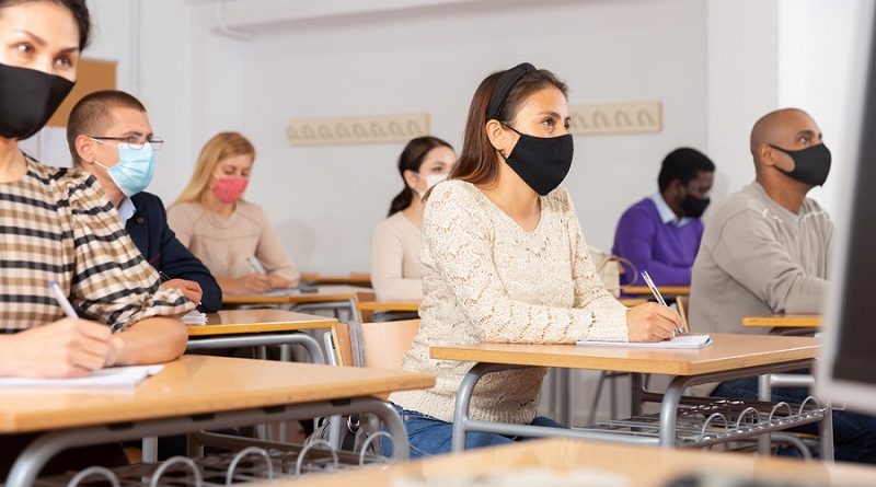 Young woman in protective face mask listening to lesson in extension school. Concept of necessary precautions and social distancing in coronavirus pandemic..