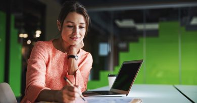 Elegant pretty Caucasian female business analyst writing something on the documents while sitting at the work desk in modern office space
